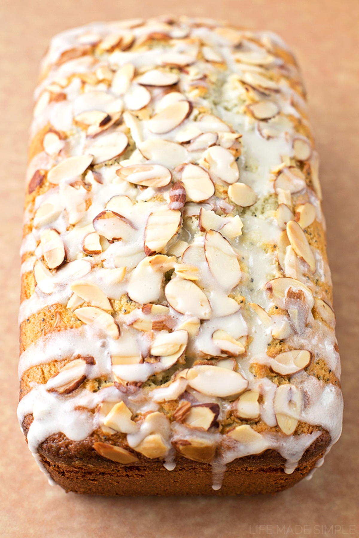 A glazed loaf of almond poppy seed bread with almond slices.