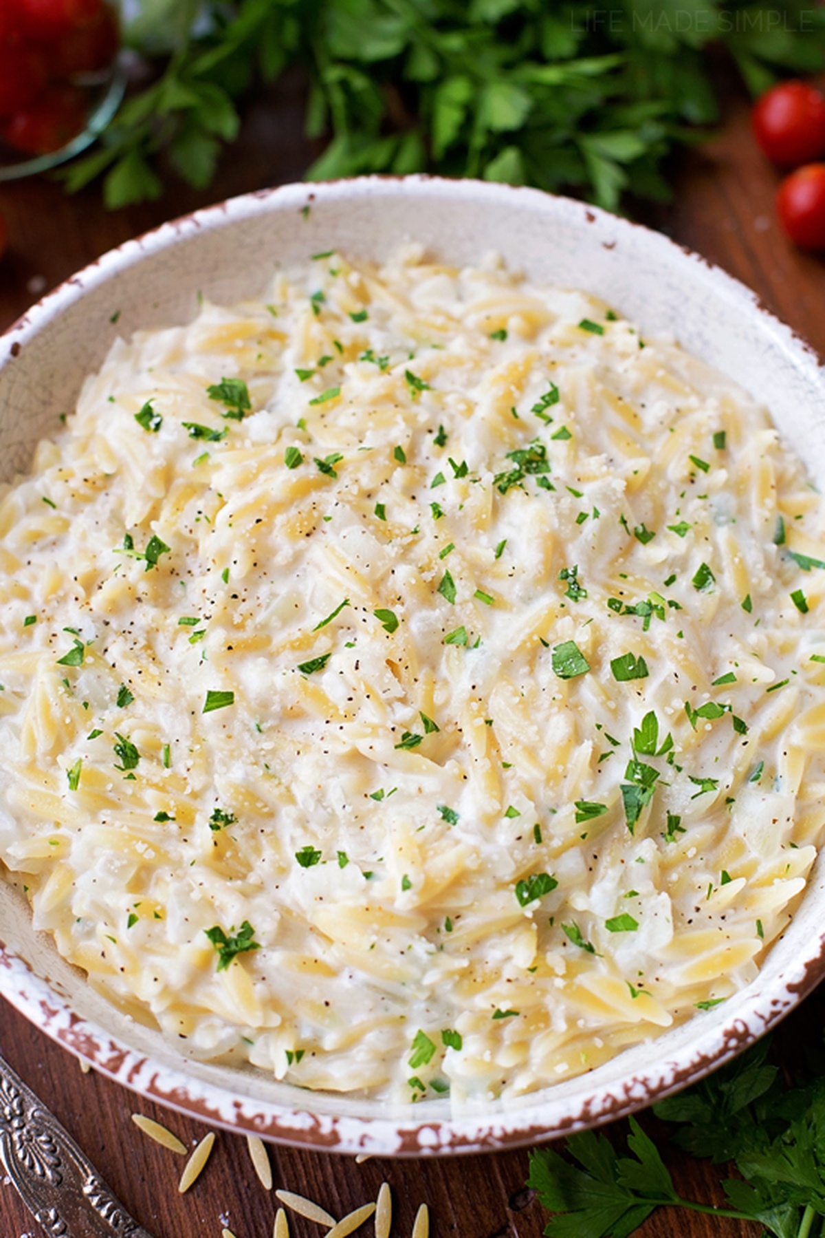 A bowl of Parmesan orzo garnished with chopped parsley on a wooden table.