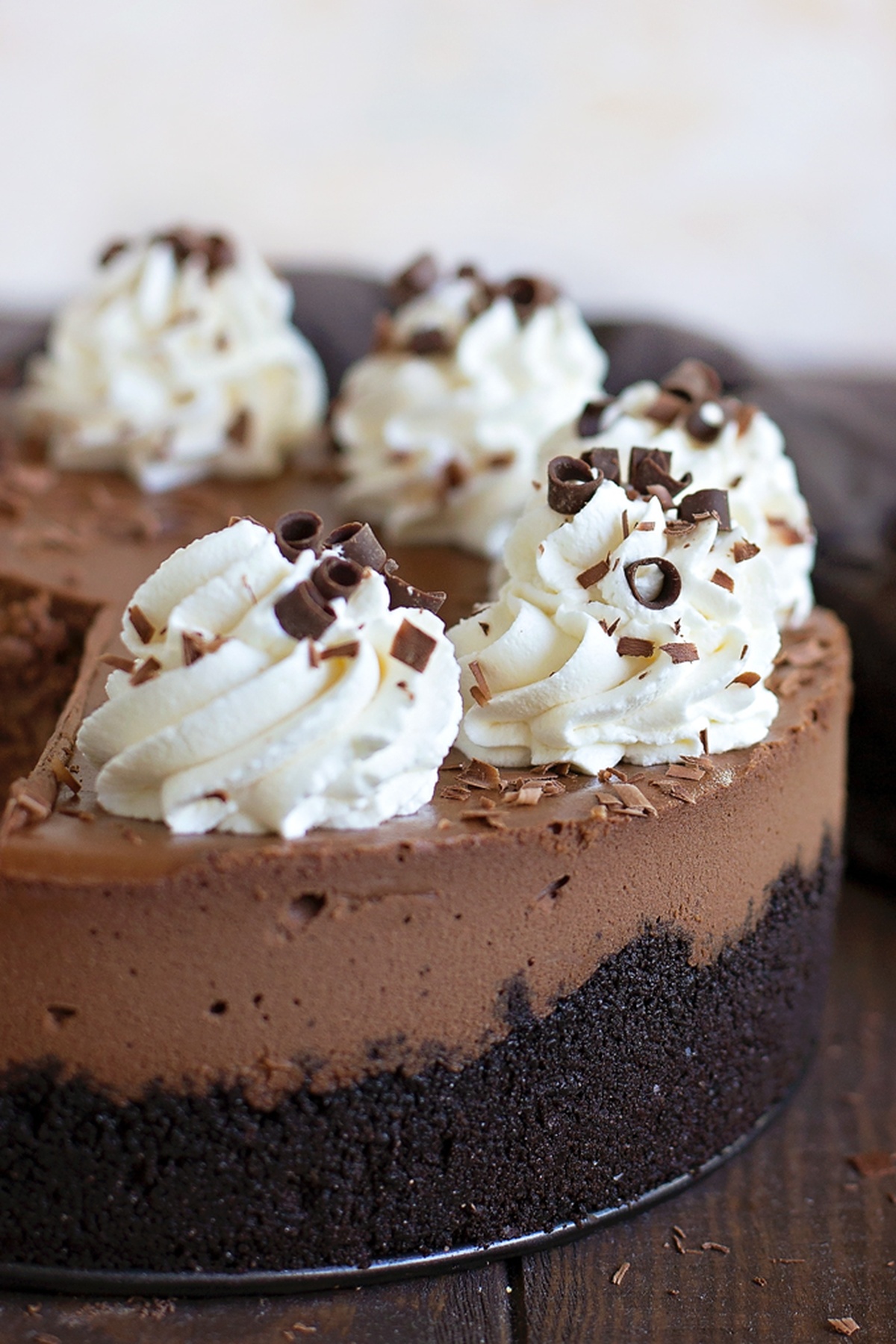 Whole chocolate cheesecake with whipped cream swirls and chocolate curls on top.