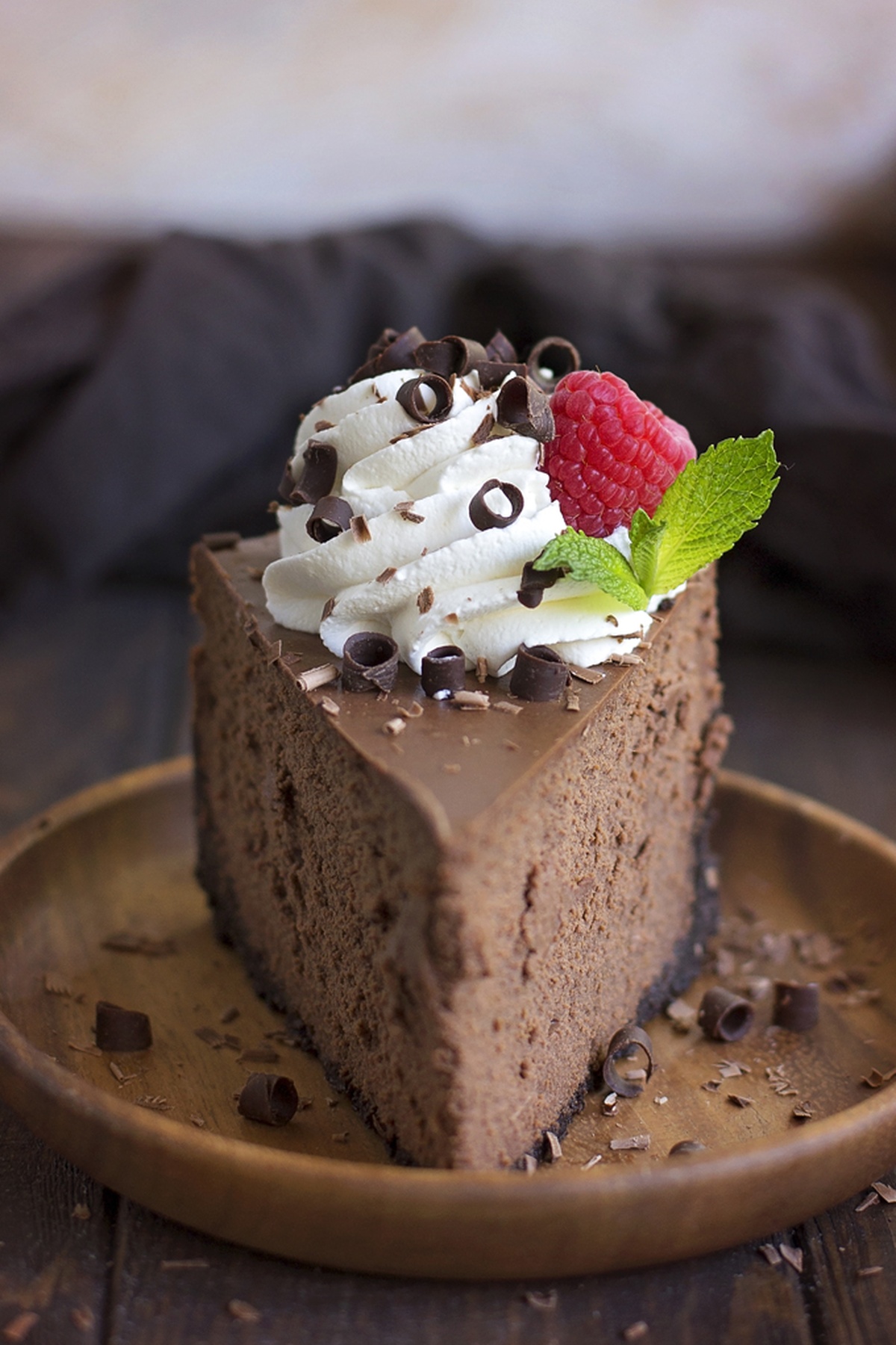 Easy chocolate cheesecake slice topped with whipped cream, chocolate curls, a fresh raspberry, and mint leaves.