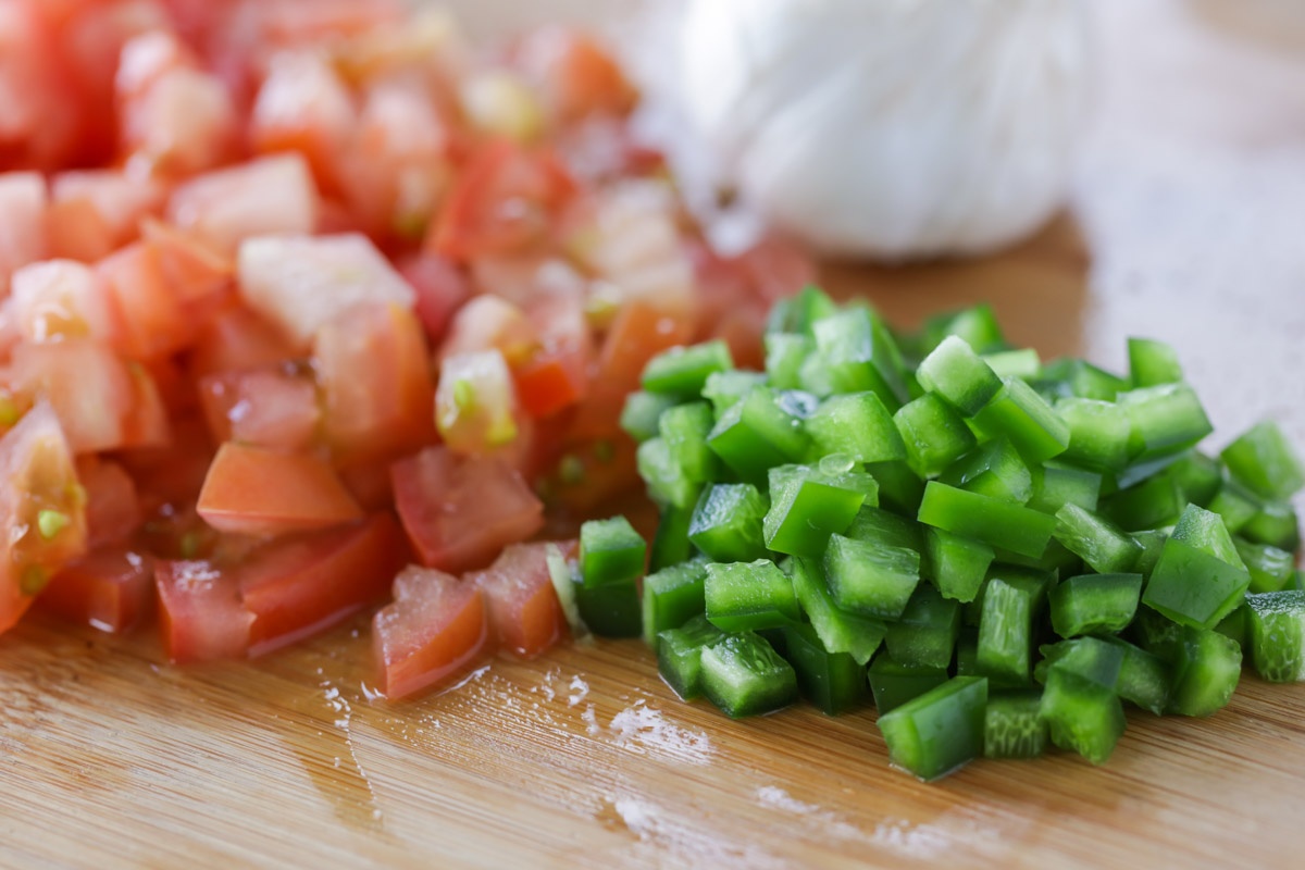 Chopped tomatoes and diced jalape&ntilde;o pepper on a wooden cutting board.