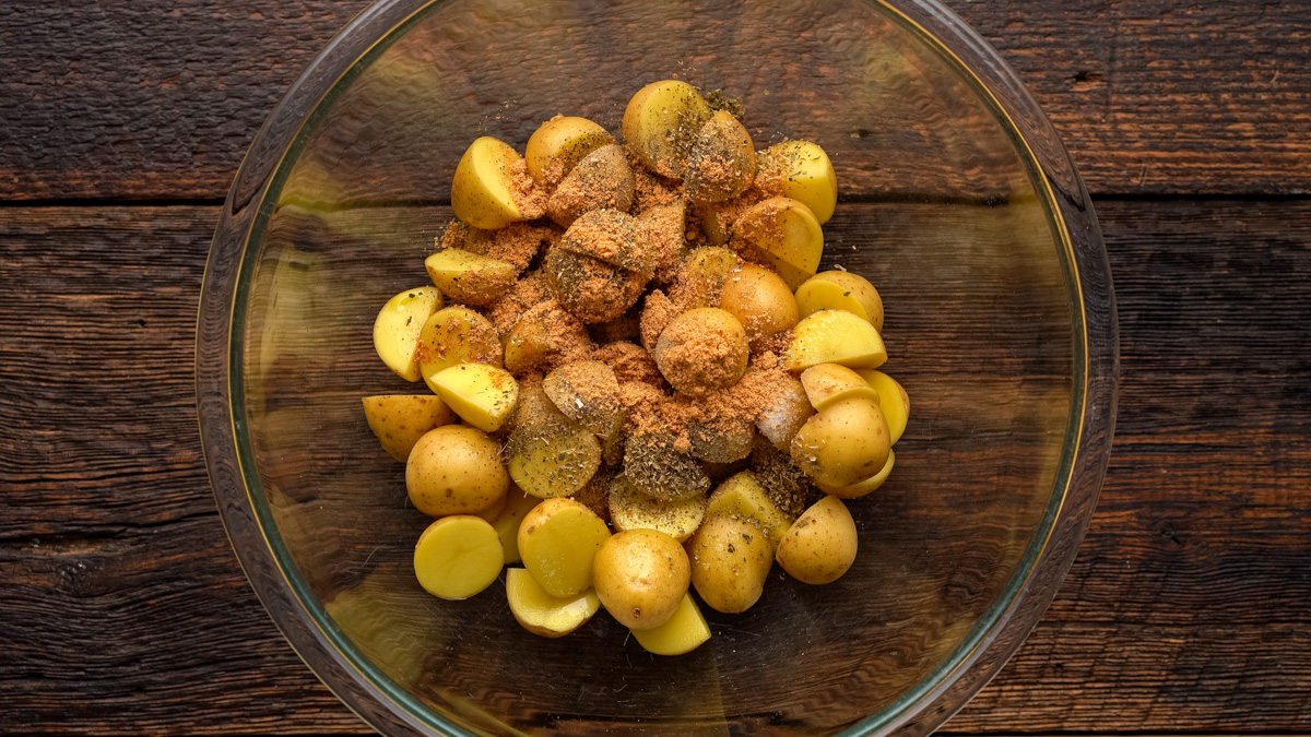 Spices and potatoes added to a glass bowl.