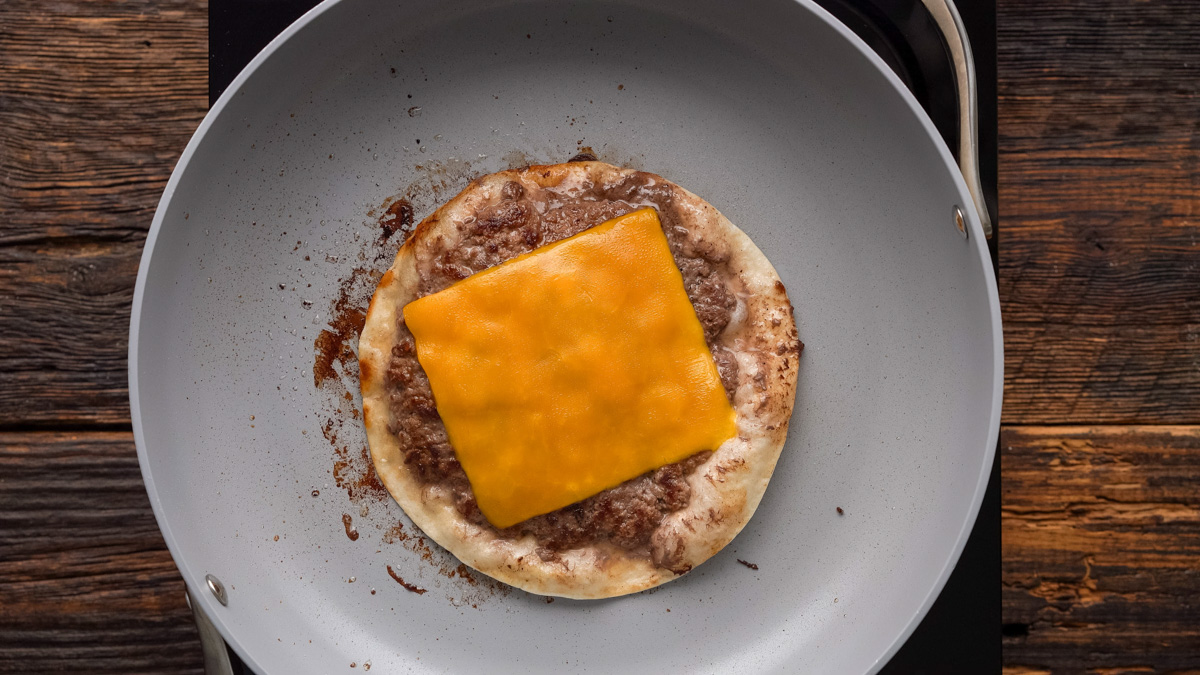 A slice of cheddar cheese added onto the cooked beef on top of the tortilla in a skillet.