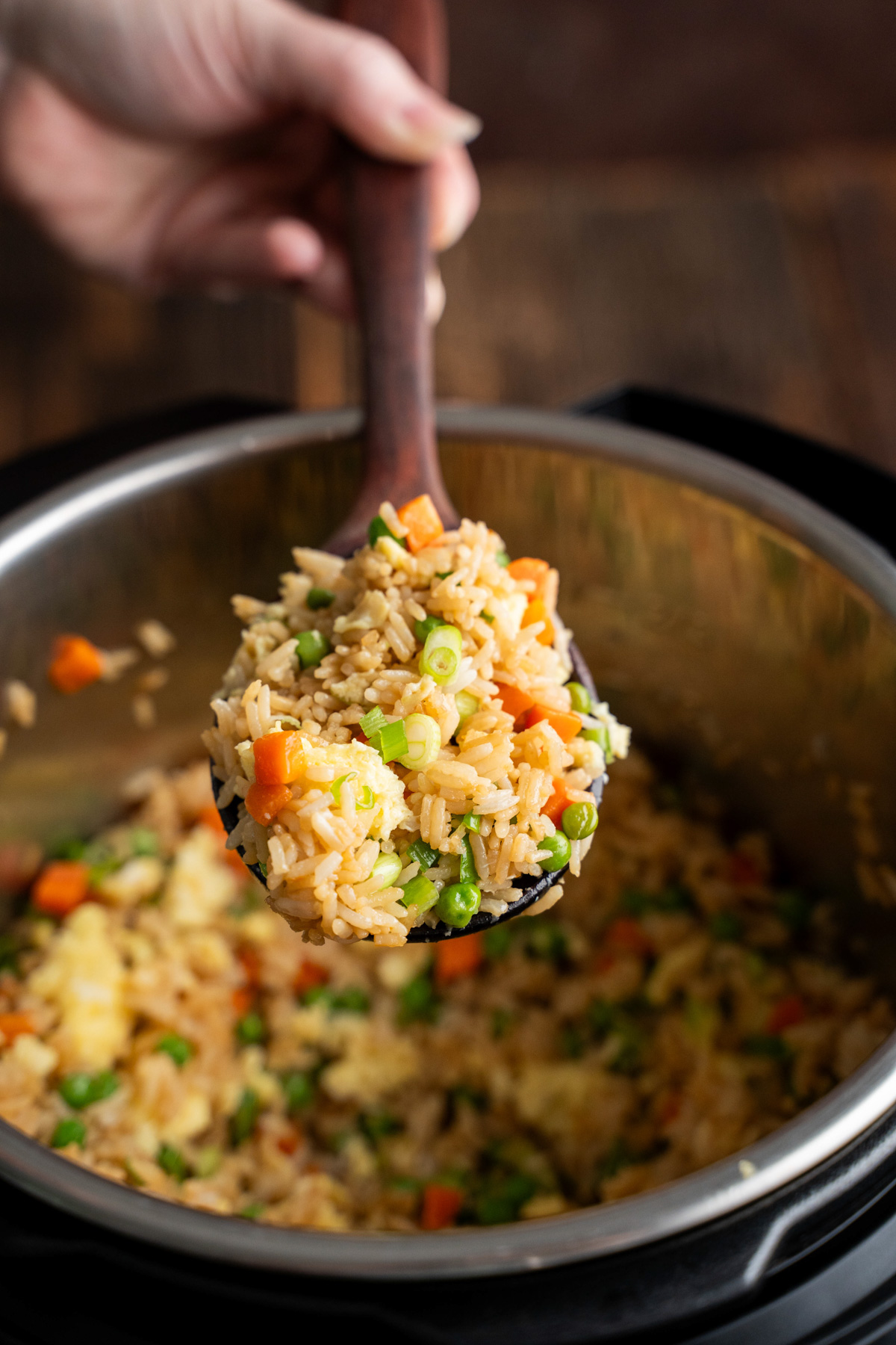 A wooden spoon filled with fried rice coming out of the Instant Pot.
