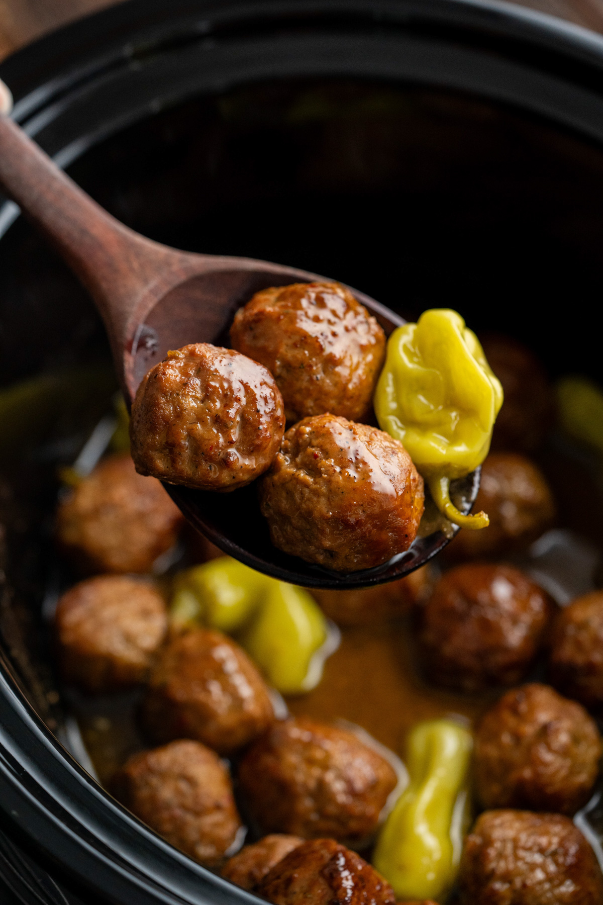 A wooden spoon with meatballs and a pepperoncini on it.