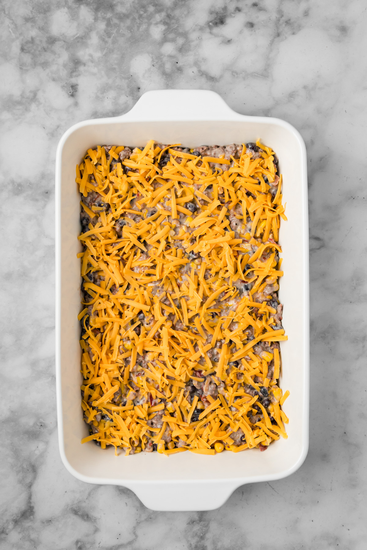 Cowboy casserole in a pan with shredded cheese on top.