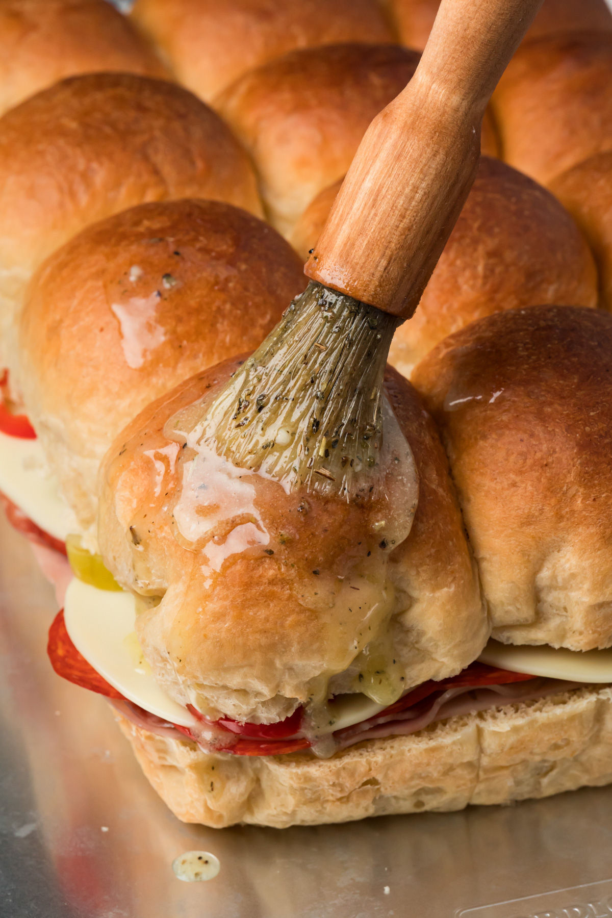 Garlic butter being brushed over the top of the sliders.