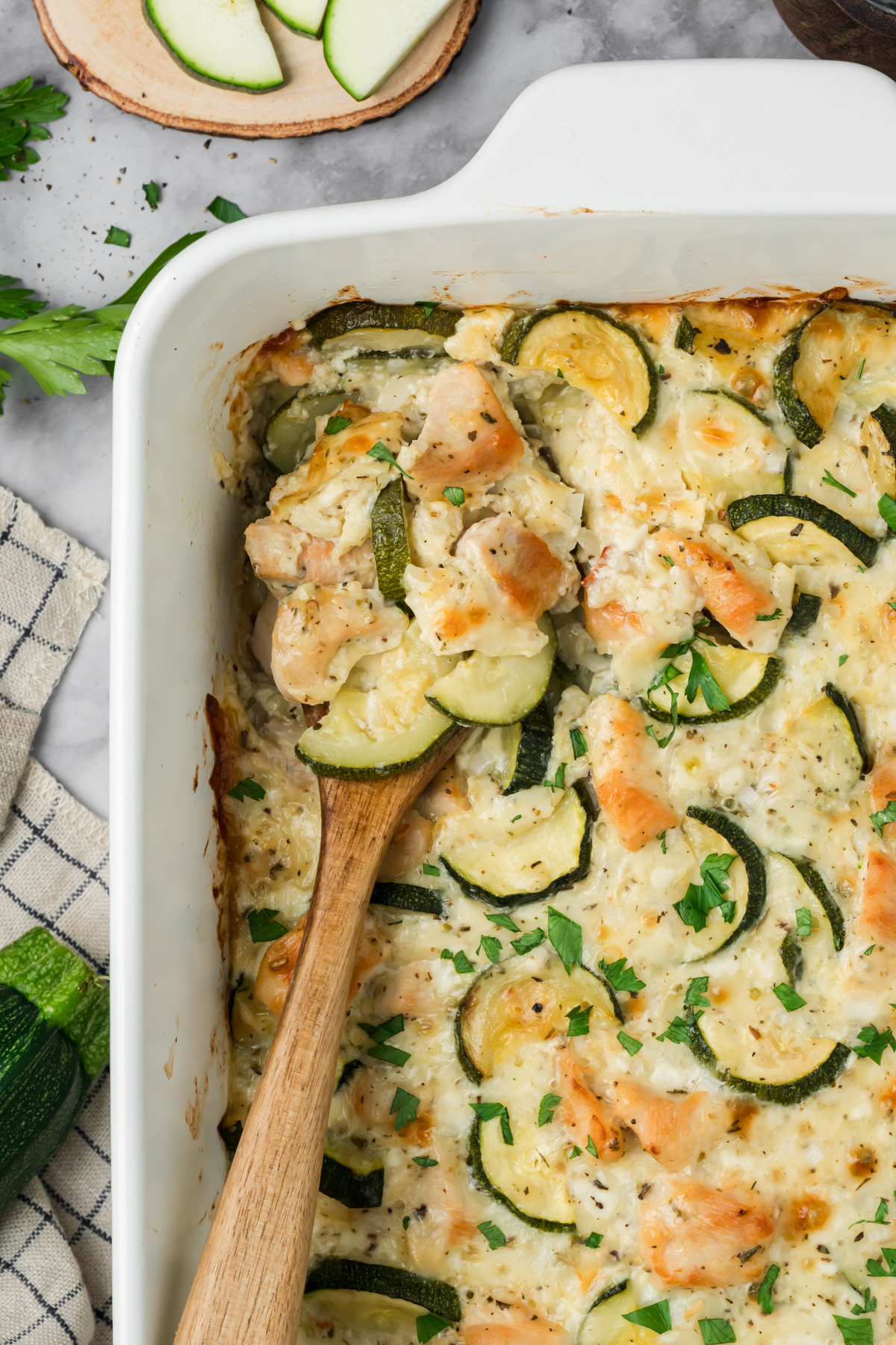 Wooden spoon in the baking dish for chicken zucchini bake.