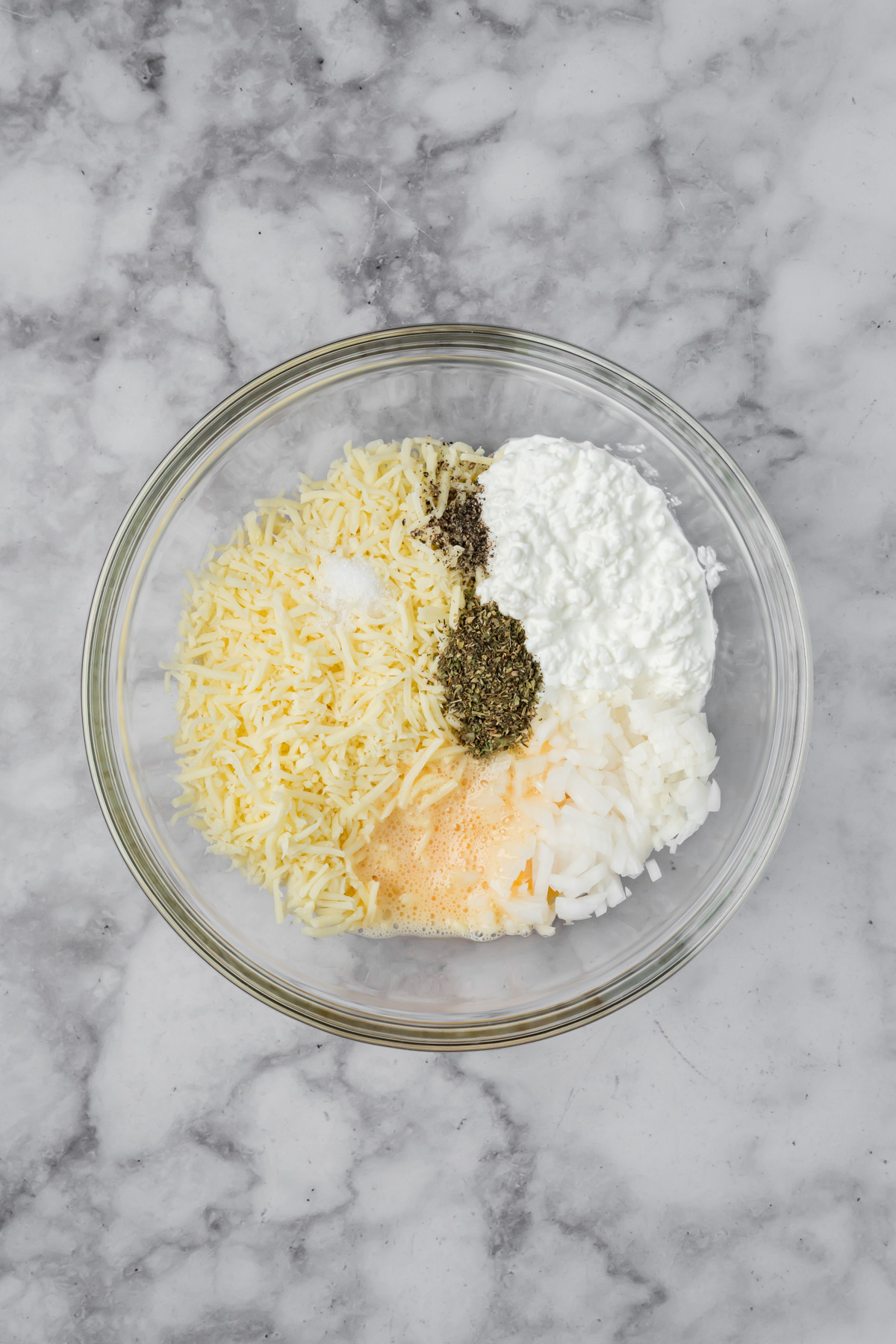 Cheese, onion, eggs, and spices in a glass bowl.