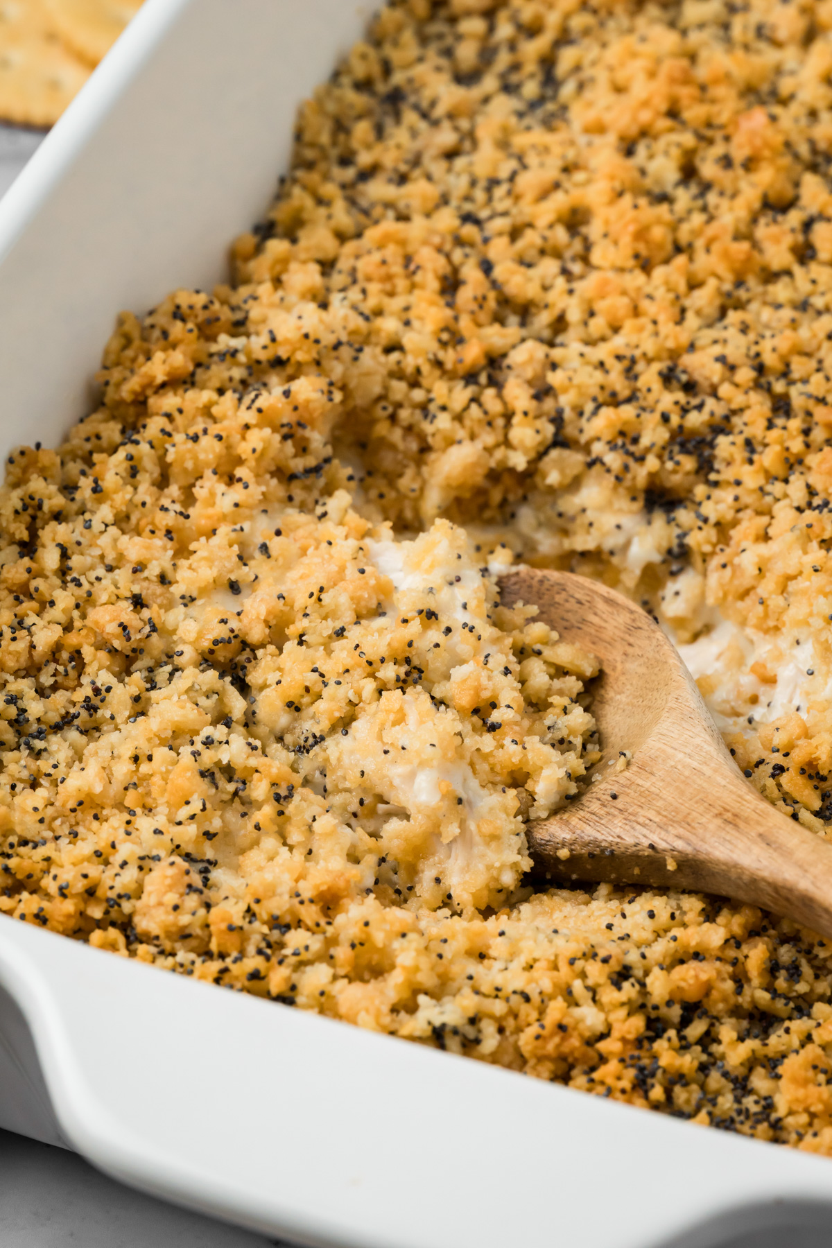 Wooden spoon scooping a serving of poppy seed chicken casserole.