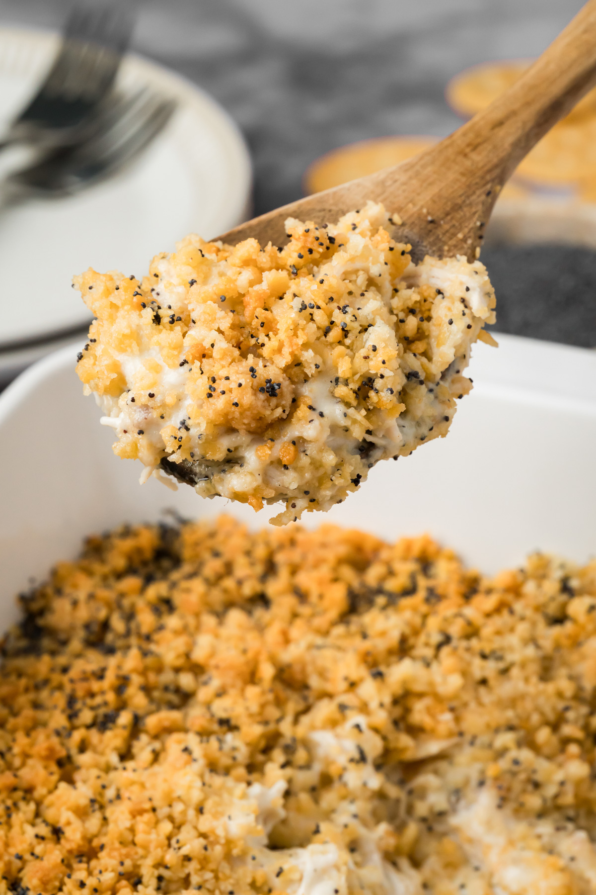 Wooden spoon of poppy seed chicken being lifted out of the baking dish.