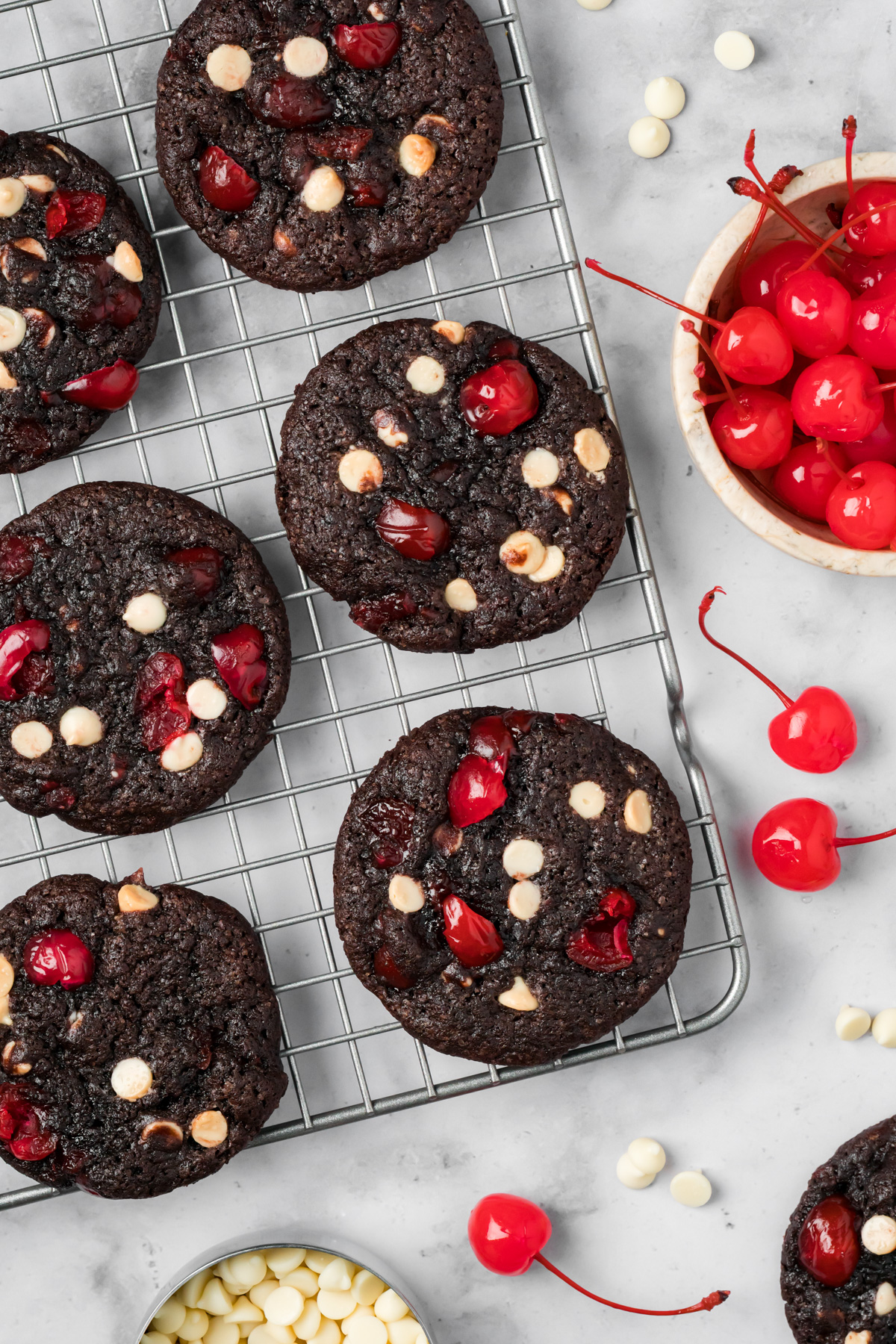 Black forest cookies on a wire rack with cherries and white chocolate chips around.